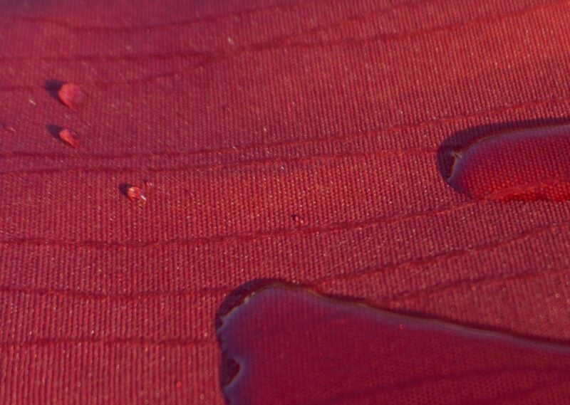 Detailaufnahme einer roten Jacquard-Tischdecke mit Wasserflecken.