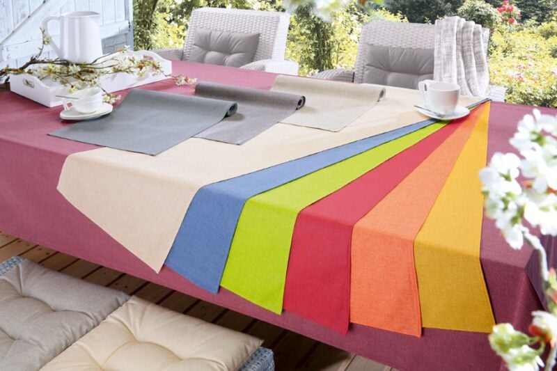 Tisch mit bunten Tischläufern in verschiedenen Farben, darunter Beige, Blau, Grün, Rot und Orange, auf einem gedeckten Tisch.