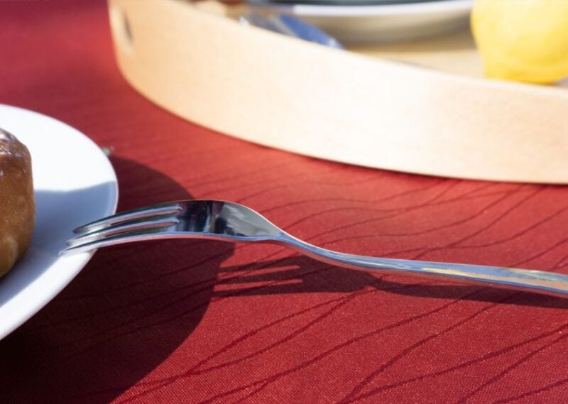 Detailaufnahme einer bordeauxfarbenen Jacquard-Tischdecke mit einer Gabel und einem Brötchen auf einem weißen Teller.