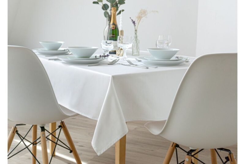 Weiße Baumwolltischdecke auf einem gedeckten Tisch mit Geschirr und Gläsern.