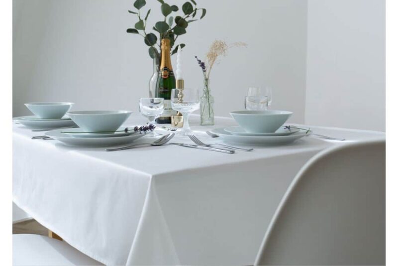 Weiße Baumwolltischdecke auf einem gedeckten Tisch mit Geschirr und Gläsern.