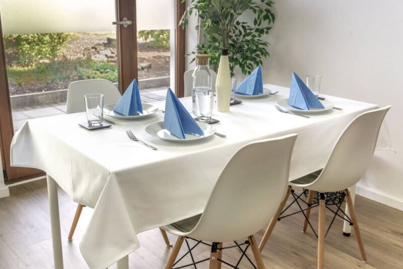 Weiße Baumwolltischdecke auf einem Tisch, gedeckt mit blauen Servietten und Gläsern.