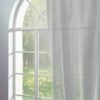 Halbtransparente, hellgraue Vorhänge vor einem großen Fenster mit Bogenform, das Tageslicht durchlässt.