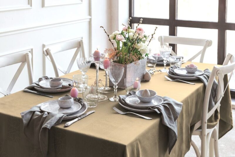 Braune Tischdecke mit floralen Elementen, rechteckig, dekoriert mit Geschirr, Gläsern und Blumenarrangement.