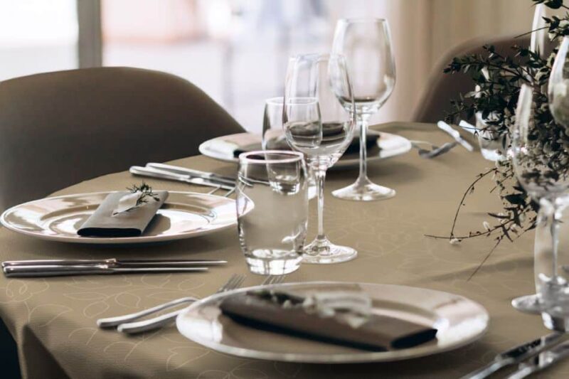 Runde, braune Tischdecke mit floralen Elementen, gedeckter Tisch mit Geschirr und Gläsern.