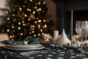 Tischdecke in Dunkelgrün mit silbernen Sternen, gedeckter Tisch für festliche Anlässe, Weihnachtsdeko im Hintergrund.