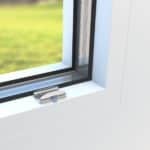 Detailaufnahme eines Fensterclips aus Metall, montiert an einem weißen Fensterrahmen.