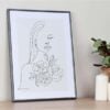 Schlichte Wandkunst mit einer stilisierten Frauenfigur und Blumen, gerahmt in einem anthrazitfarbenen Kunststoffrahmen.