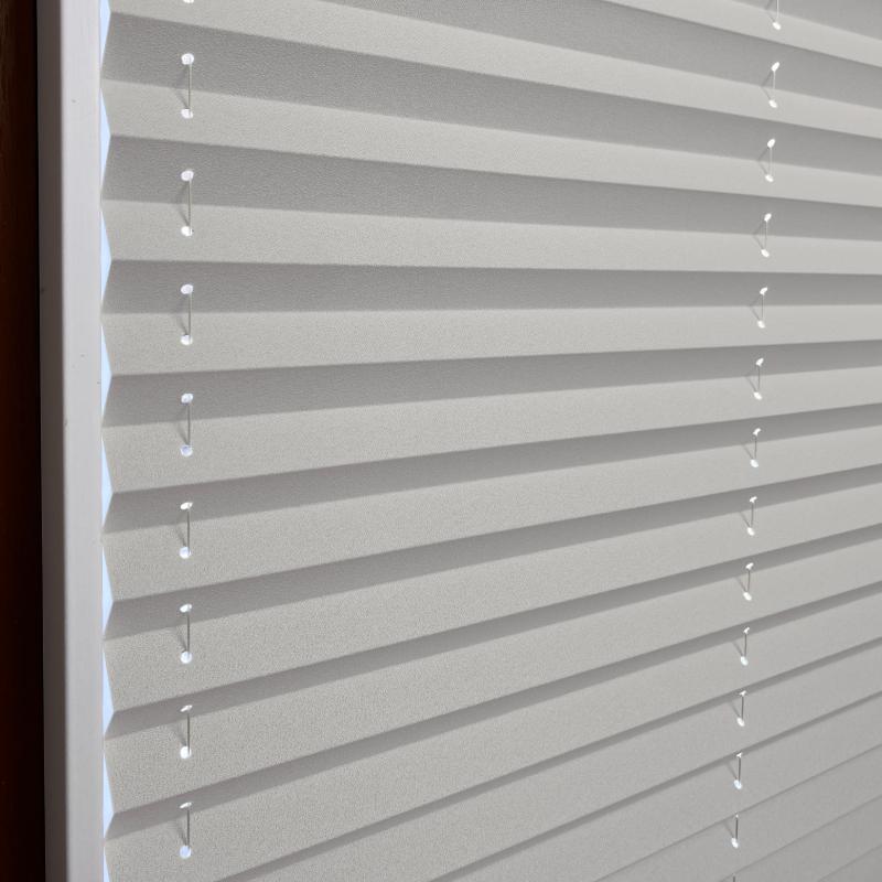 Hellgraues Plissee mit strukturierten Falten und transparenten Schnüren zur Lichtregulierung.