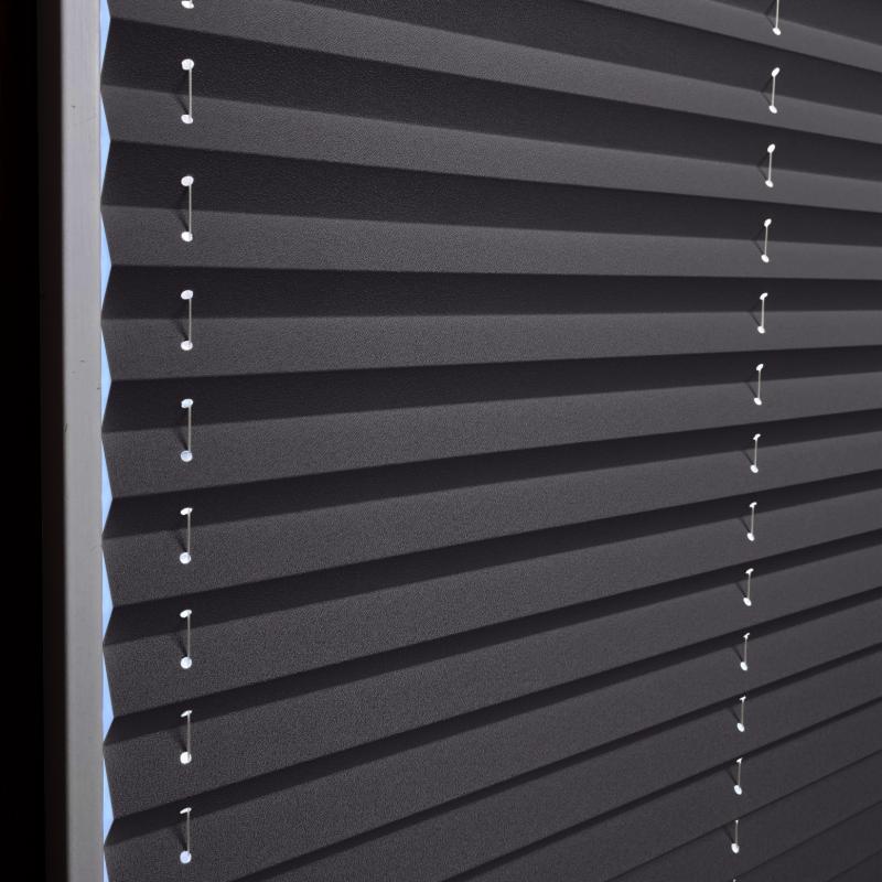 Plissee in Schwarz mit strukturiertem Material und weißen Halterungen, ideal für Lichtregulierung und Sichtschutz.