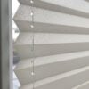 Detailaufnahme eines blickdichten Plissees in hellem Beige mit strukturierten Falten und weißen Zugbändern.