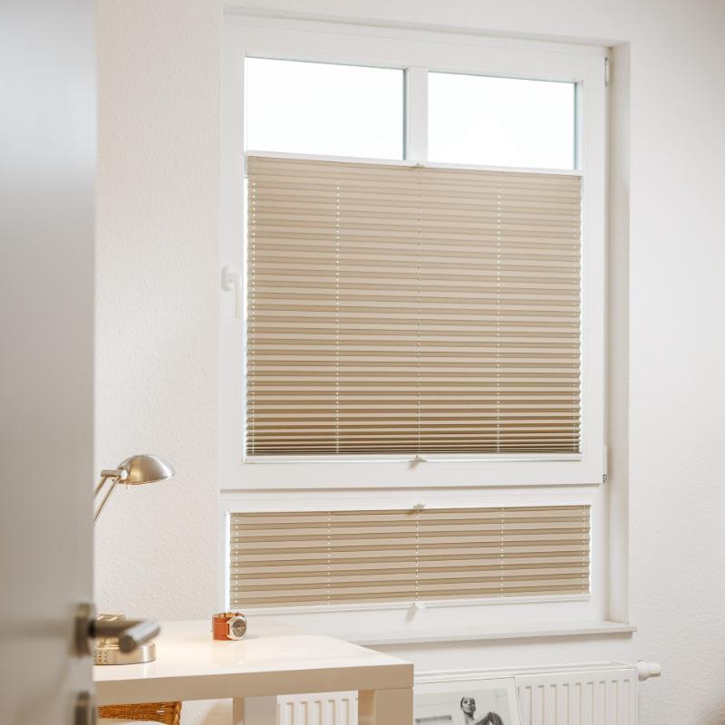Hellbeige Plissee mit horizontalen Lamellen vor einem Fenster.