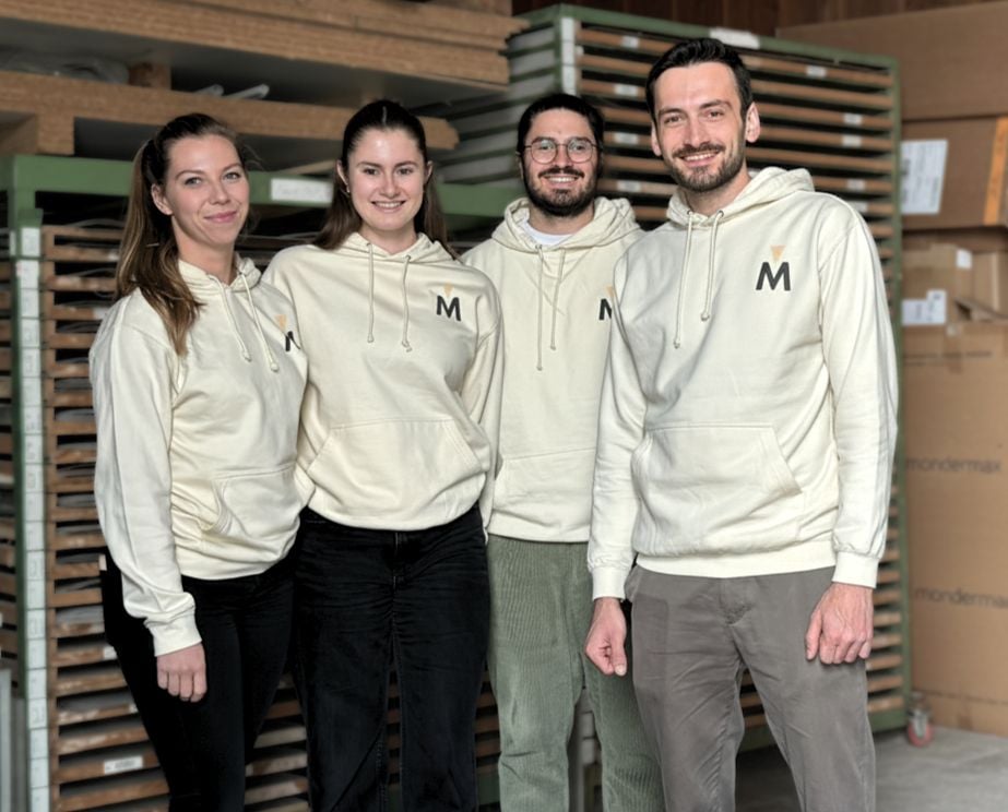 Vier Personen in weißen Hoodies mit "M"-Logo, stehend im Lager.